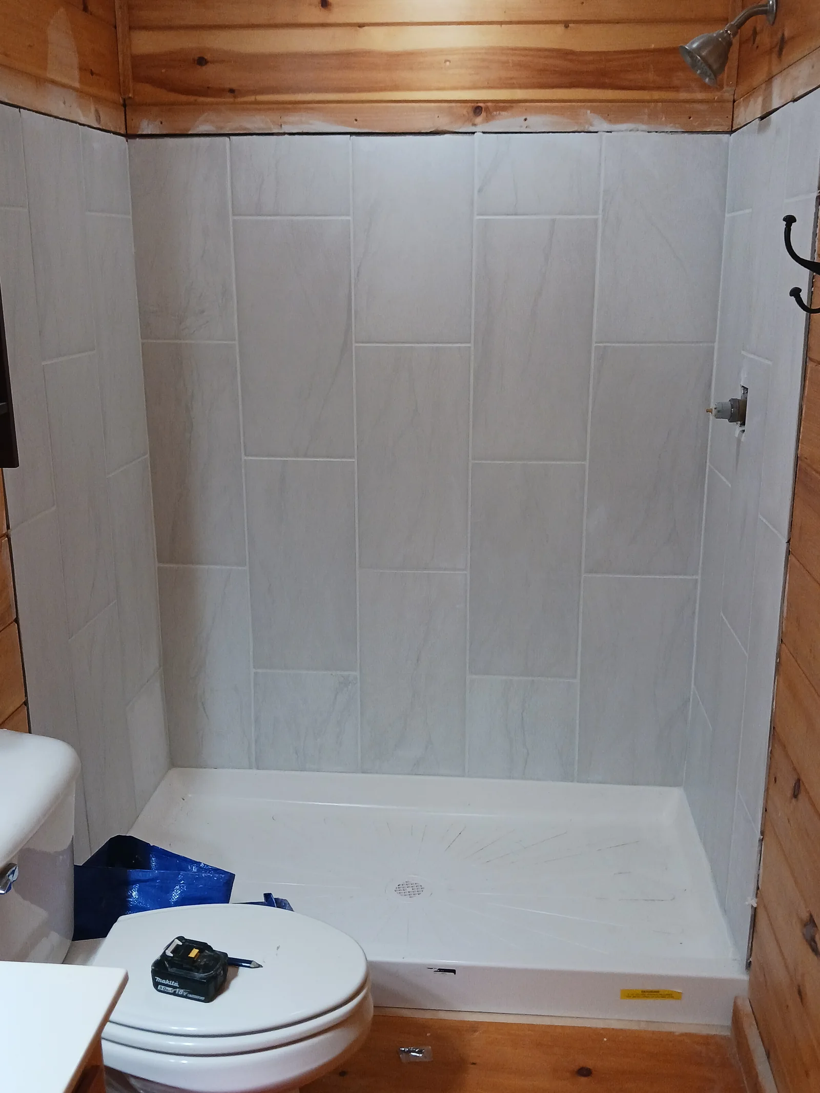 Light tiled shower and white base beside warm wood walls in a cabin bathroom