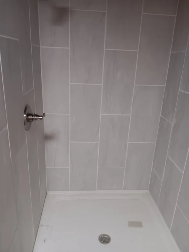 Gray tiled shower with white base and installed chrome handle