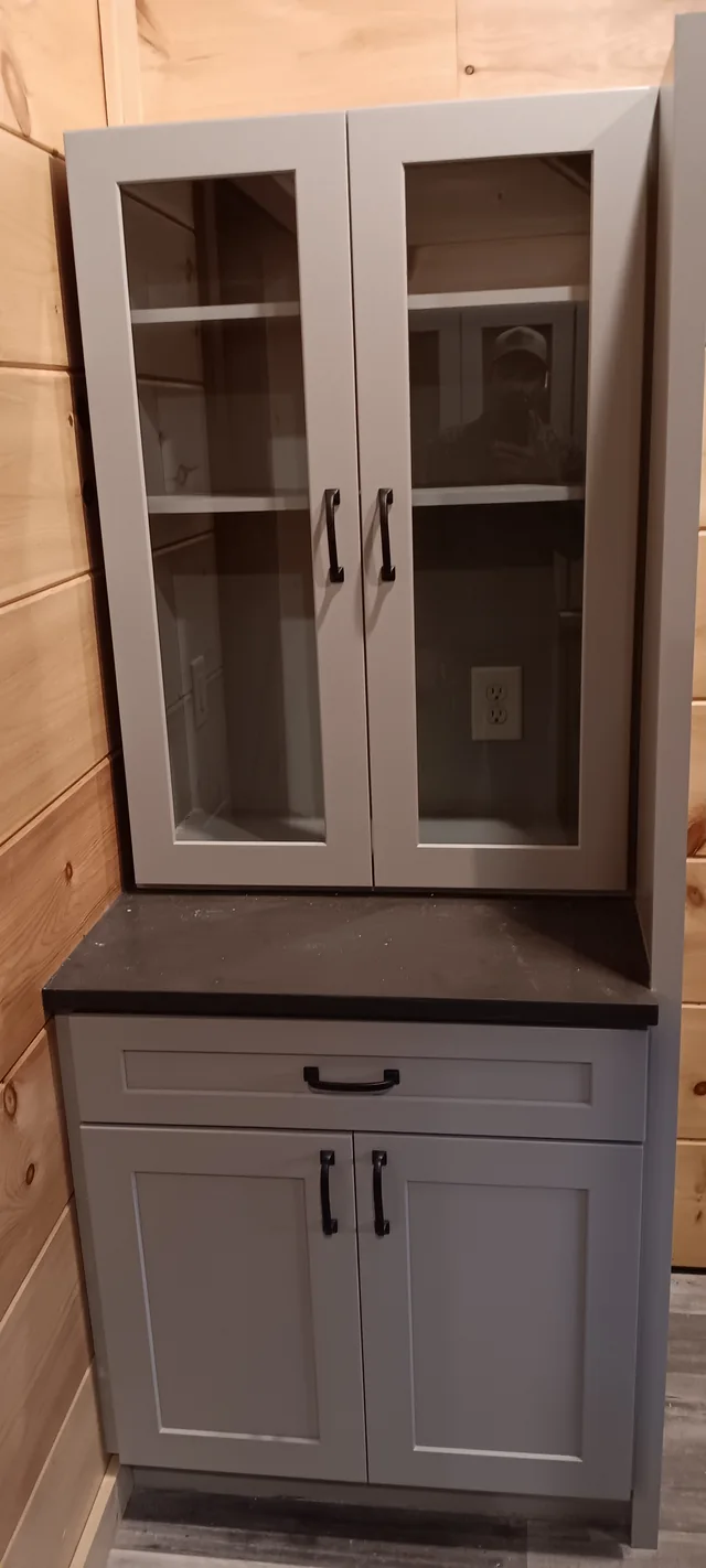 Gray glass-front storage cabinet with lower drawers against wood-paneled walls
