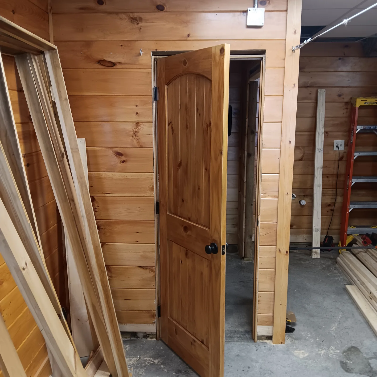 Wood-paneled room with a wood door and trim being fitted around the opening